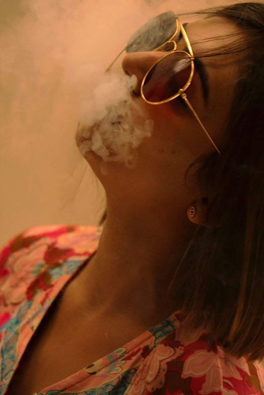 Woman in Gold Sunglasses Exhaling Smoke in Warm Ambient Light HD phone wallpaper