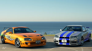 Orange Toyota Supra and Silver Nissan Skyline GT-R parked side by side on a coastal road HD wallpaper
