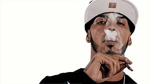 Anuel AA Portrait Smoking Cigar With White Cap and Black Shirt HD wallpaper
