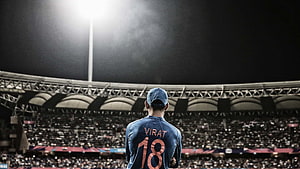 Virat Kohli in Blue Jersey Standing Before Cricket Stadium Crowd at Night HD wallpaper