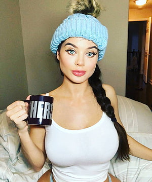 Lana Rhoades in a light blue knit beanie holding a Hers mug while seated on a bed HD phone wallpaper
