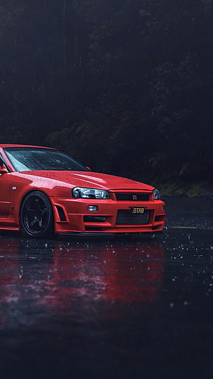 Red Nissan Skyline GT-R R34 parked on wet asphalt in the rain with dark forest background HD phone wallpaper